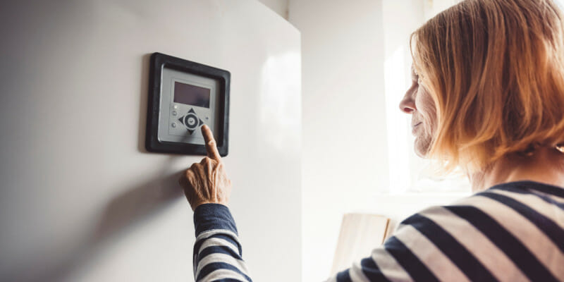 woman using thermostat mounted on the wall