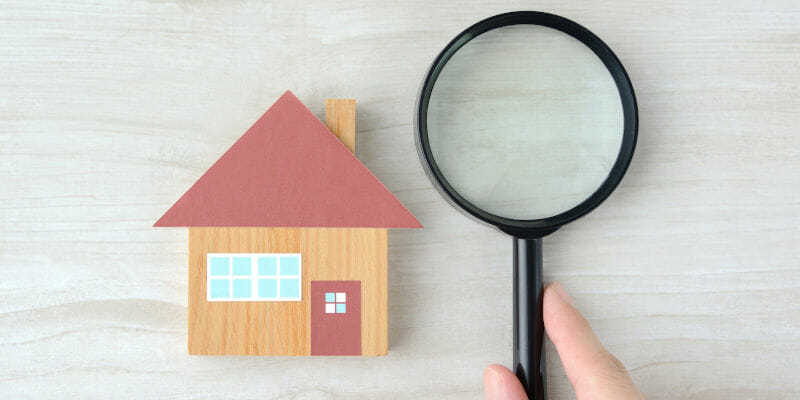 House object and human's hands with magnifying glass on natural wooden table